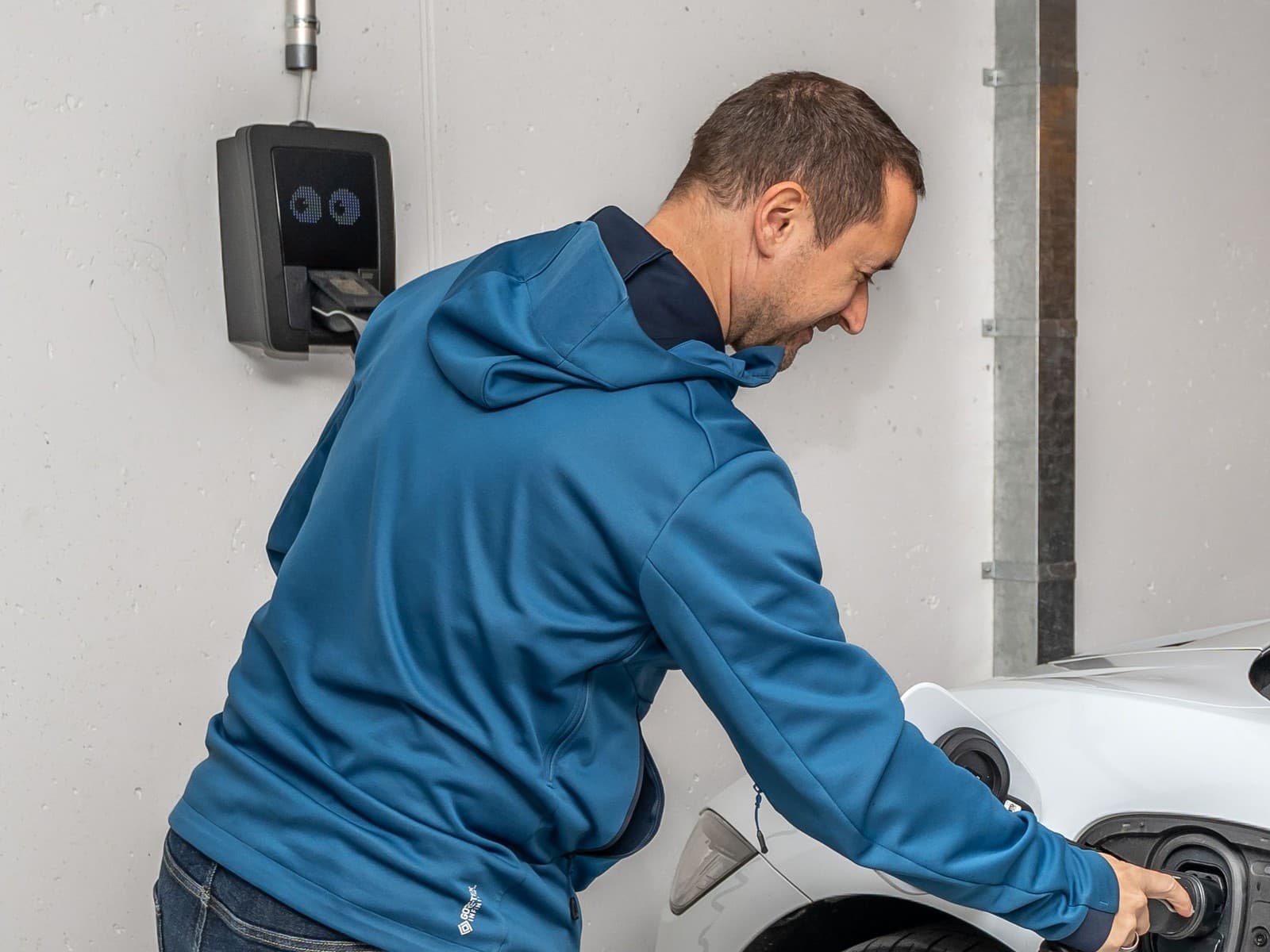 Pessoa conectando o cabo do carregador de parede ao carro elétrico em uma garagem residencial